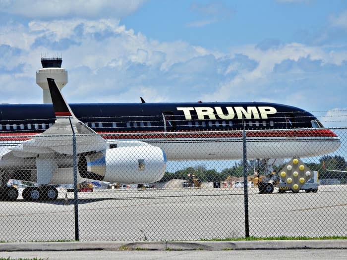 Private pitchy  with "TRUMP" connected  the side, parked connected  an airdrome  tarmac down  a chain-link obstruction   nether  a cloudy sky