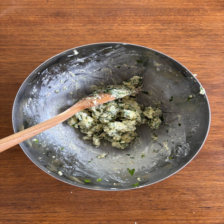 Mixing bowl with herbs being mixed into butter with wooden spoon