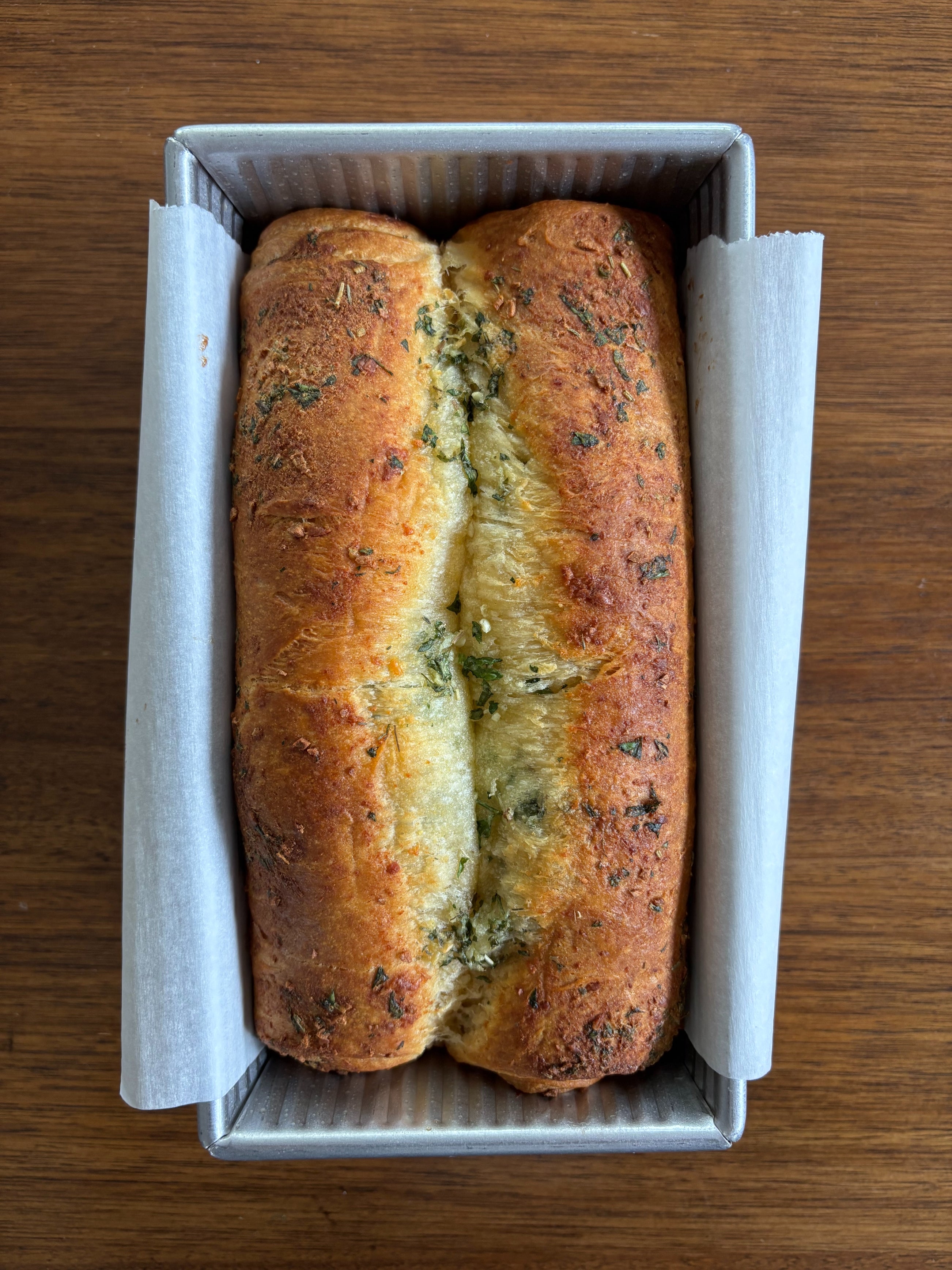 Loaf of herb bread in a parchment-lined loaf pan