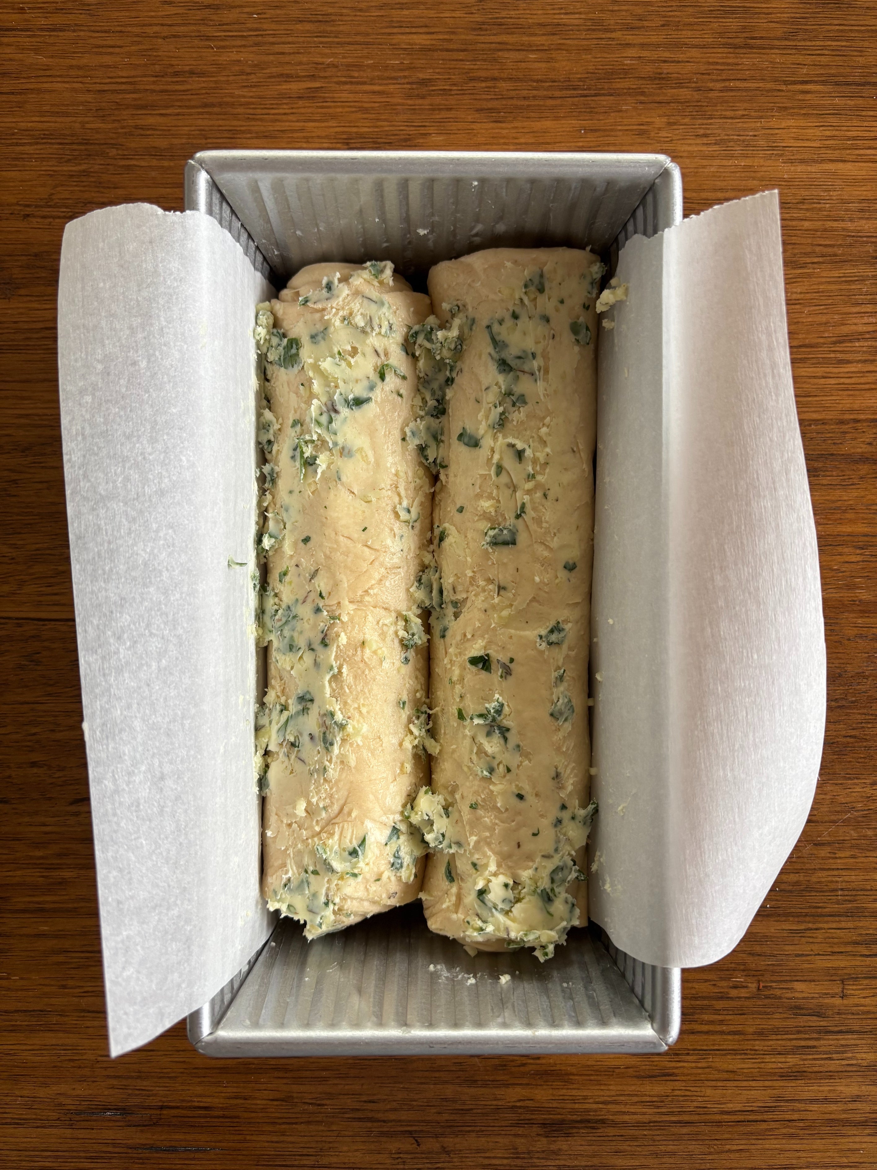 Herb-topped dough in a parchment-lined loaf pan