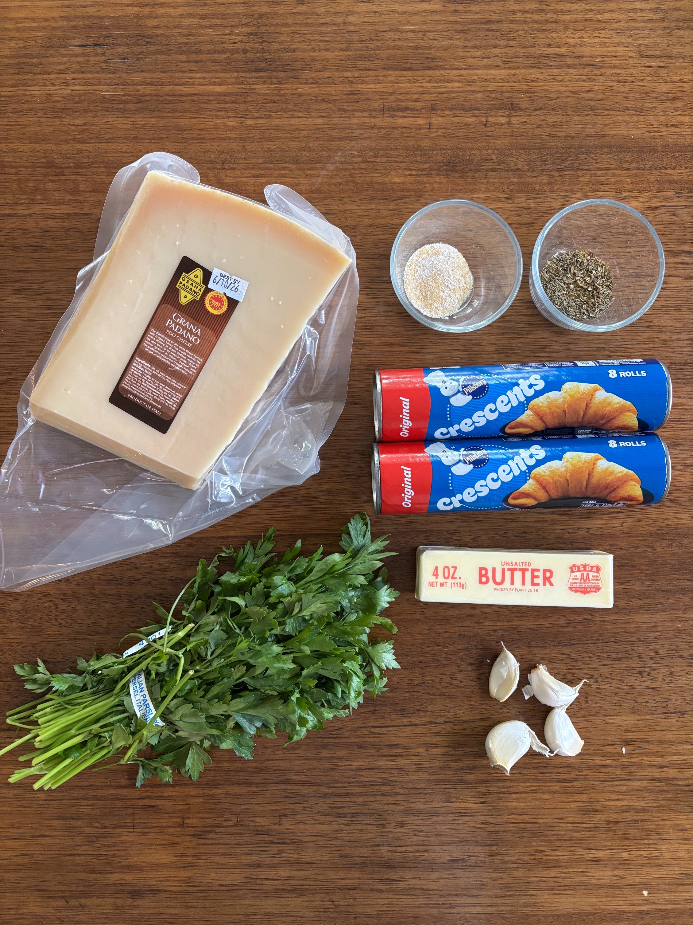 Cheese, garlic, parsley, butter, crescent roll dough, and spices are arranged on a wooden surface