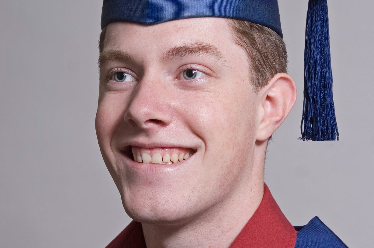 A graduate smiles, wearing a cap and gown, facing slightly away from the camera