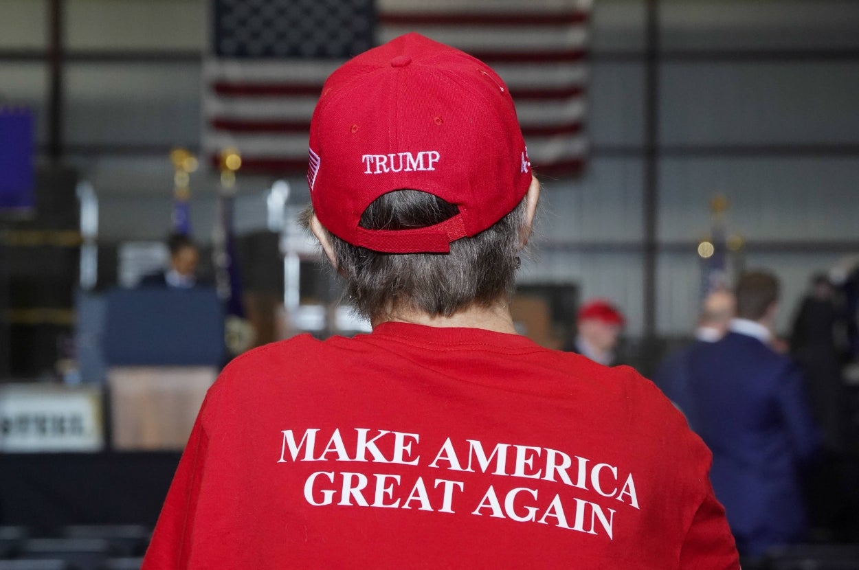 Person in a "Make America Great Again" hat and shirt at an indoor event with U.S. flags in the background