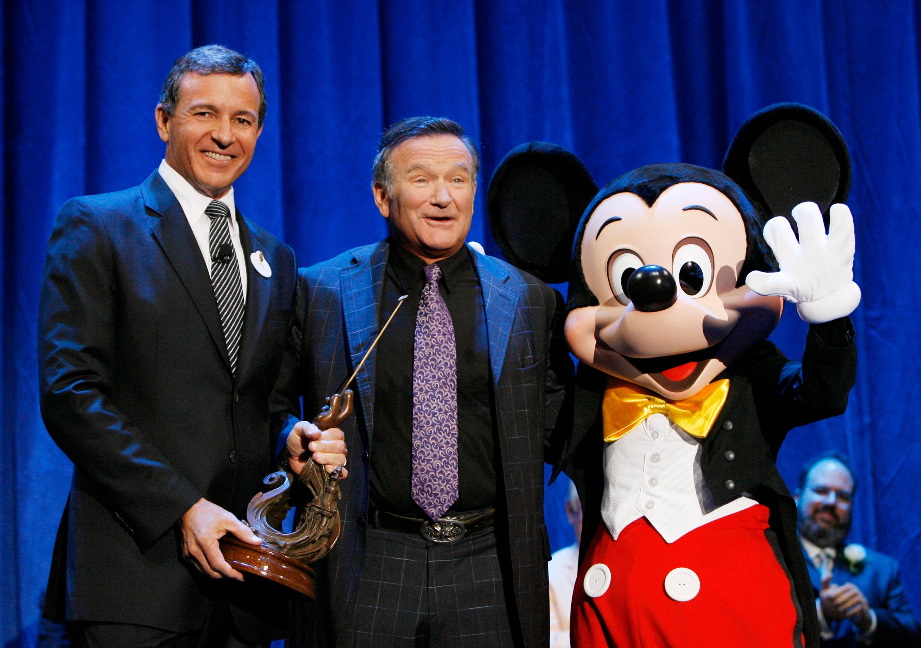 Three individuals basal   together, including a idiosyncratic   successful  a Mickey Mouse costume. The idiosyncratic   successful  the mediate  smiles warmly portion    the different   holds a statue