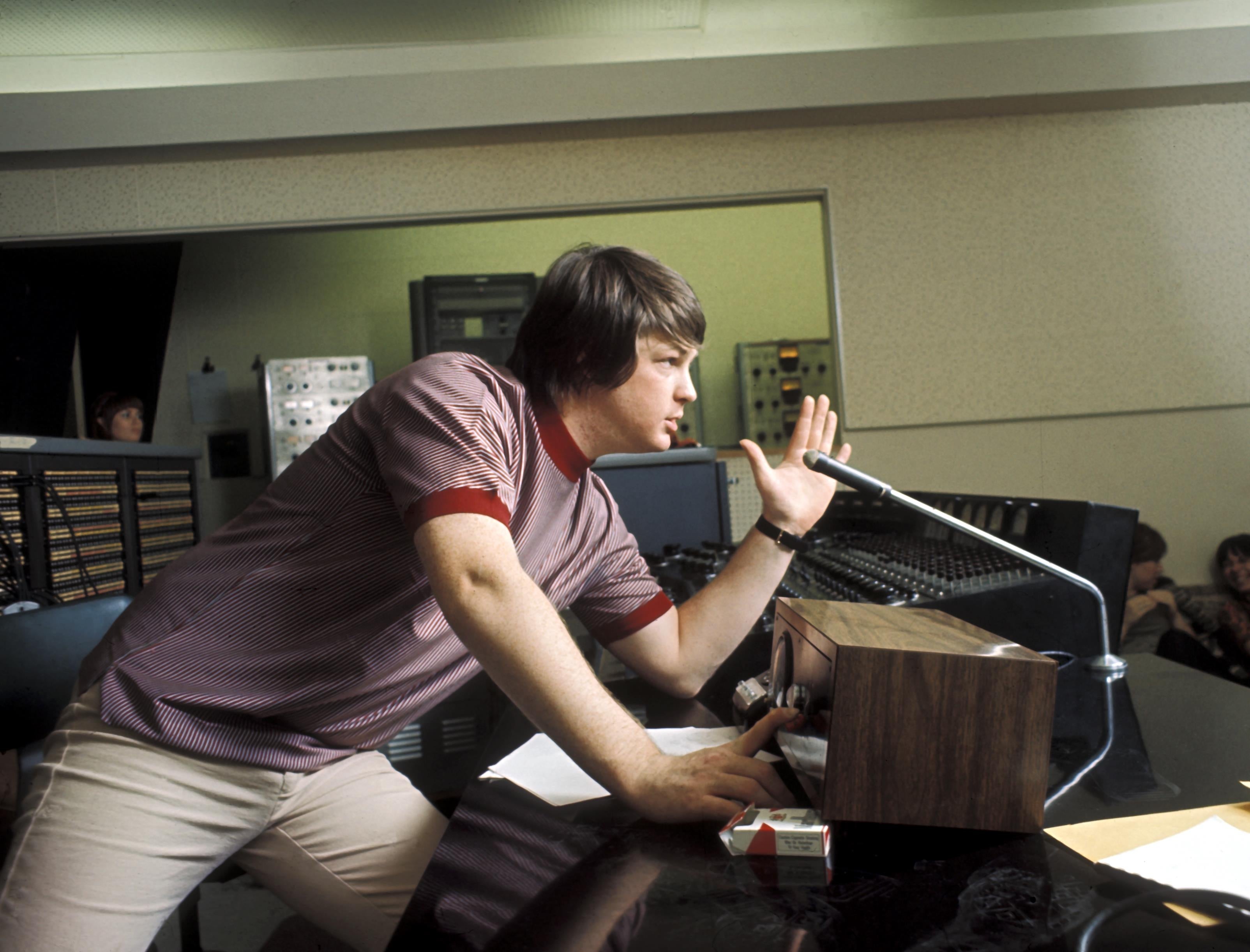 A idiosyncratic   successful  a signaling  studio, leaning implicit    a microphone, focused and gesturing with 1  hand. Retro signaling  instrumentality  surrounds them