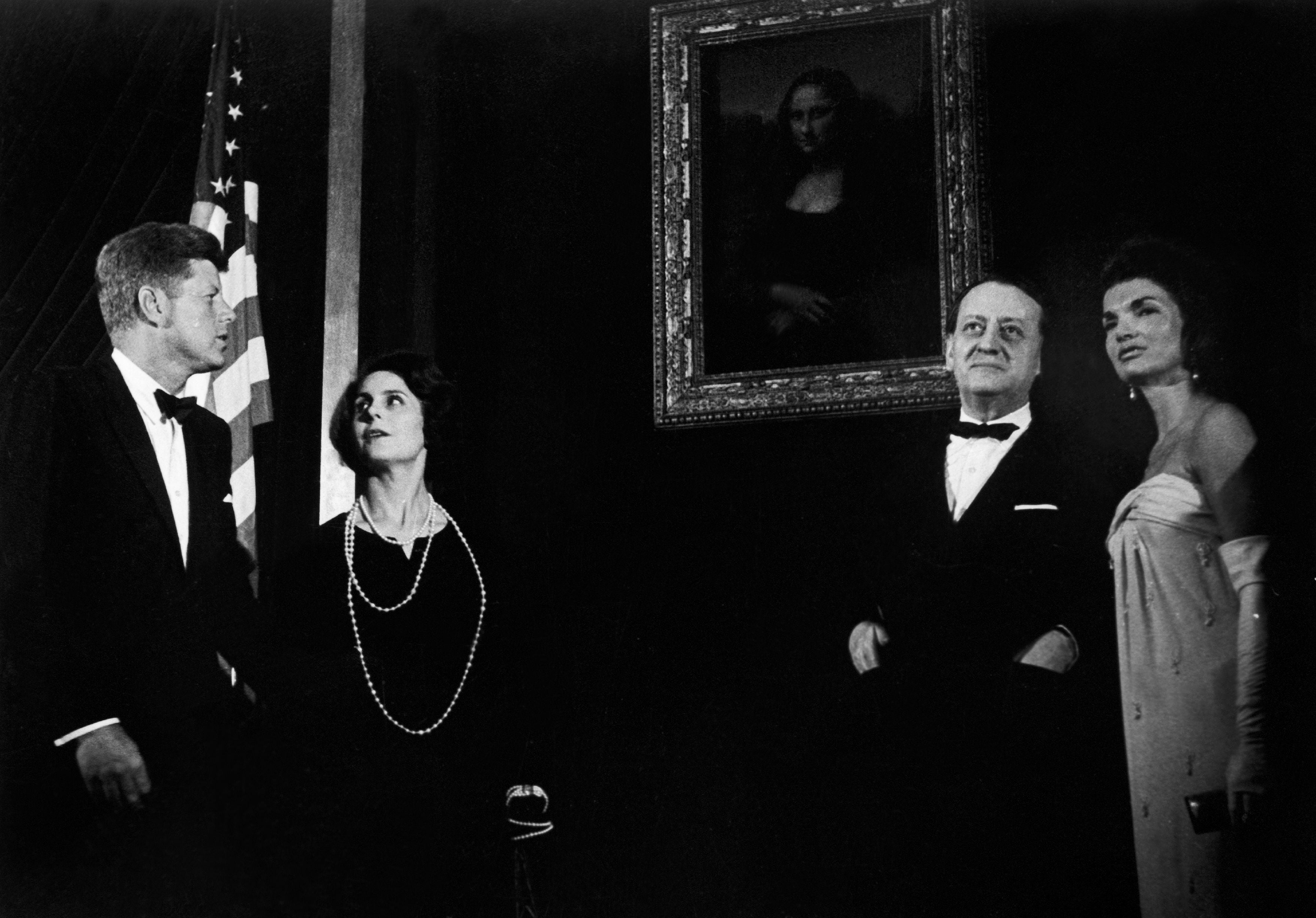 People successful  ceremonial  attire look   astatine  the Mona Lisa painting; an American emblem  is successful  the background