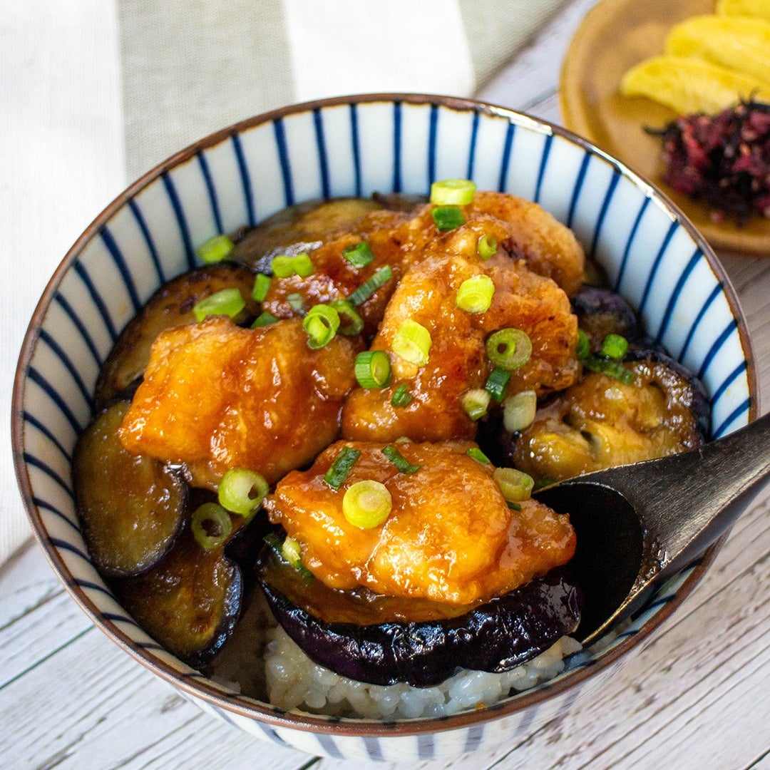 ご飯に盛られた揚げナスと甘辛ソースのから揚げ。刻みネギが上に載せられ、箸が添えられています。
