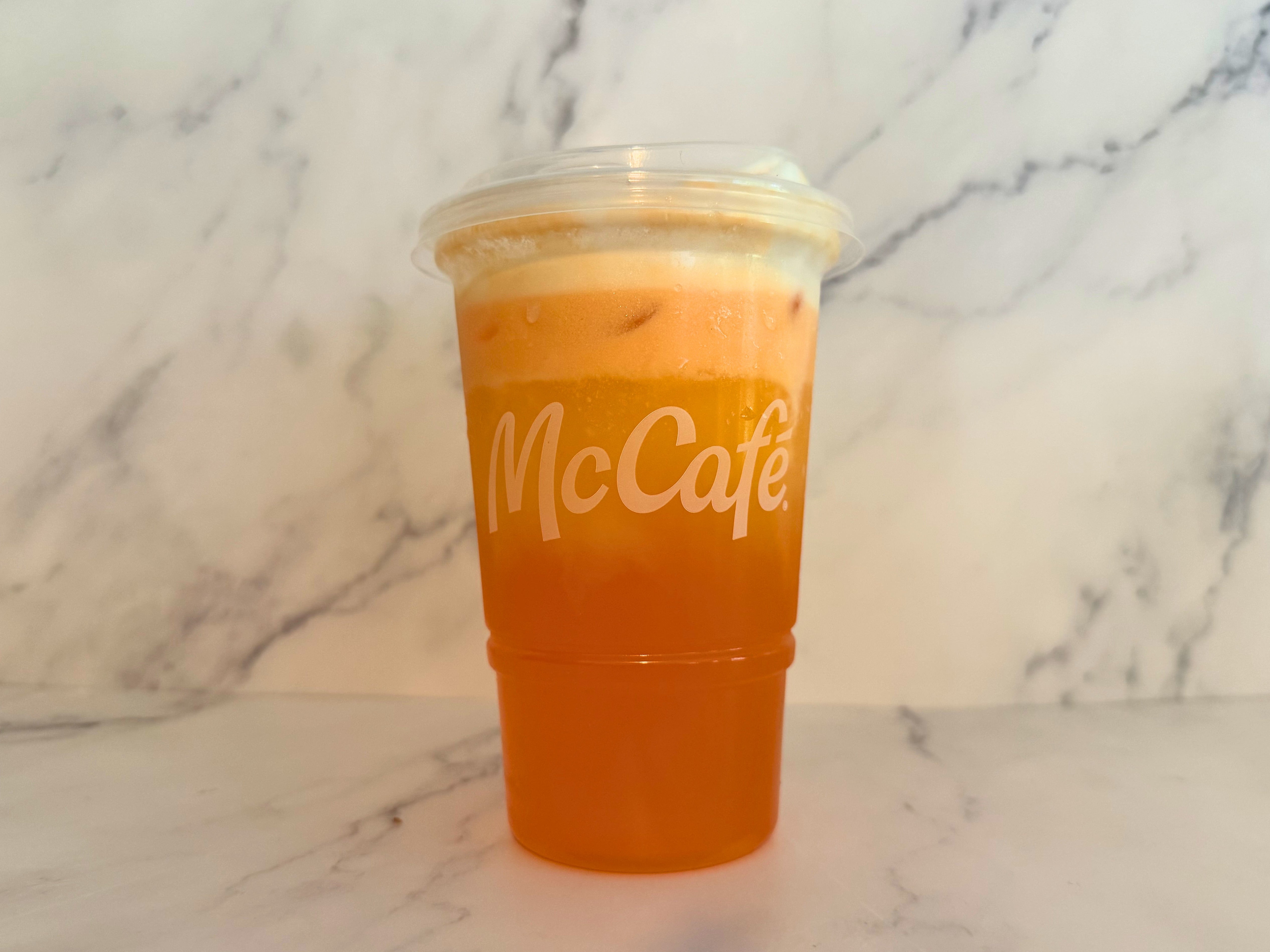 A clear plastic cup of McCafé Orange Dream with foam on top on a marble surface