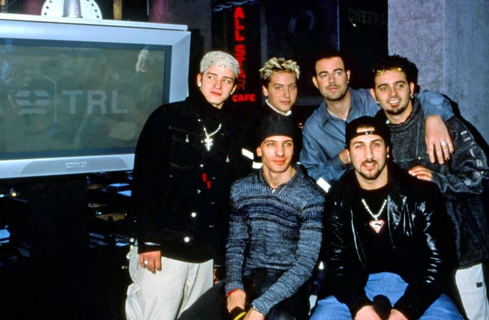 Large group of people with stylish late 90s fashion posed in front of a "TRL" TV screen