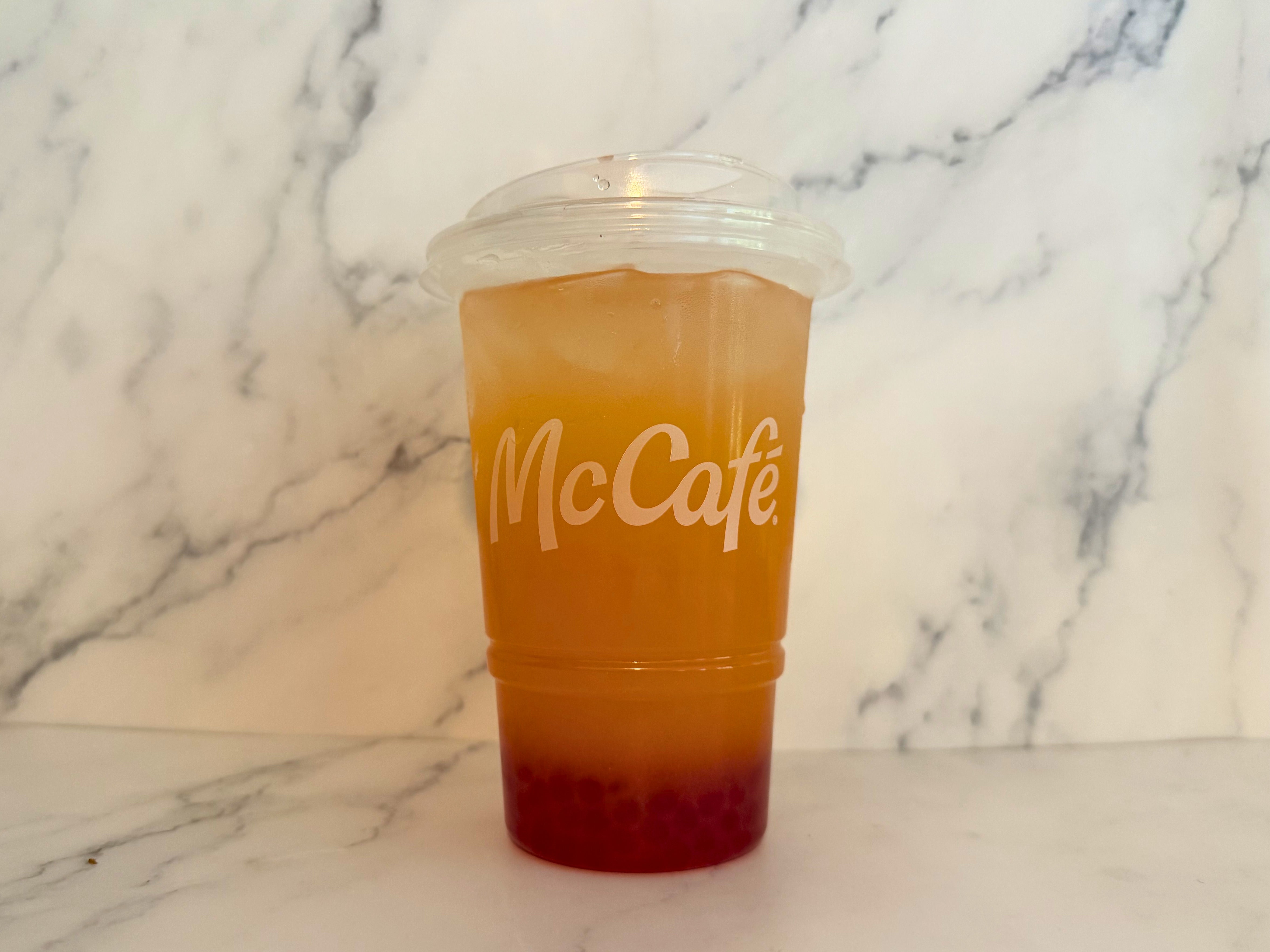 McCafé cup with Mango Pineapple Refresher and strawberry boba balls at the bottom on a marble surface