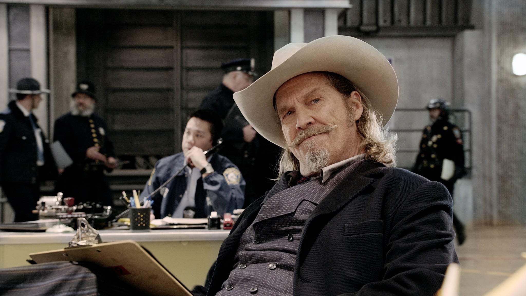 A idiosyncratic   wearing a cowboy chapeau  and suit   sits successful  a engaged  office, with constabulary  officers and desks successful  the background