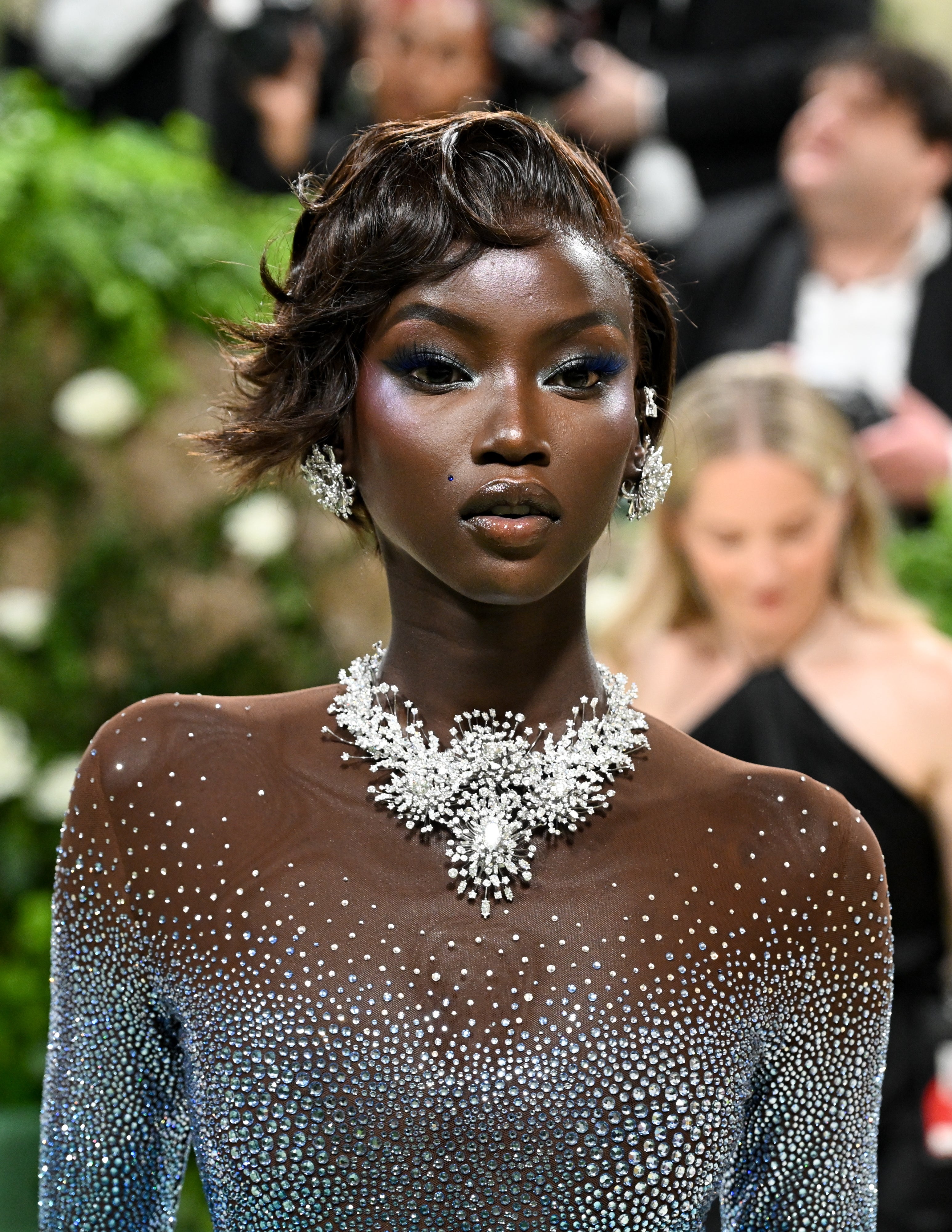 Anok Yai connected reddish carpet successful a sparkling, jewel-encrusted gown with ornate matching jewelry, surrounded by photographers and greenery