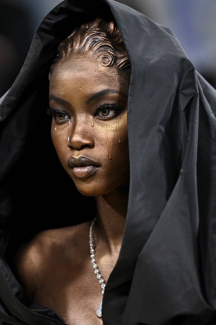 Anok Yai with melodramatic  oculus  constitution  and tears detail, wearing a hood and a diamond necklace, exudes elegance and mystery