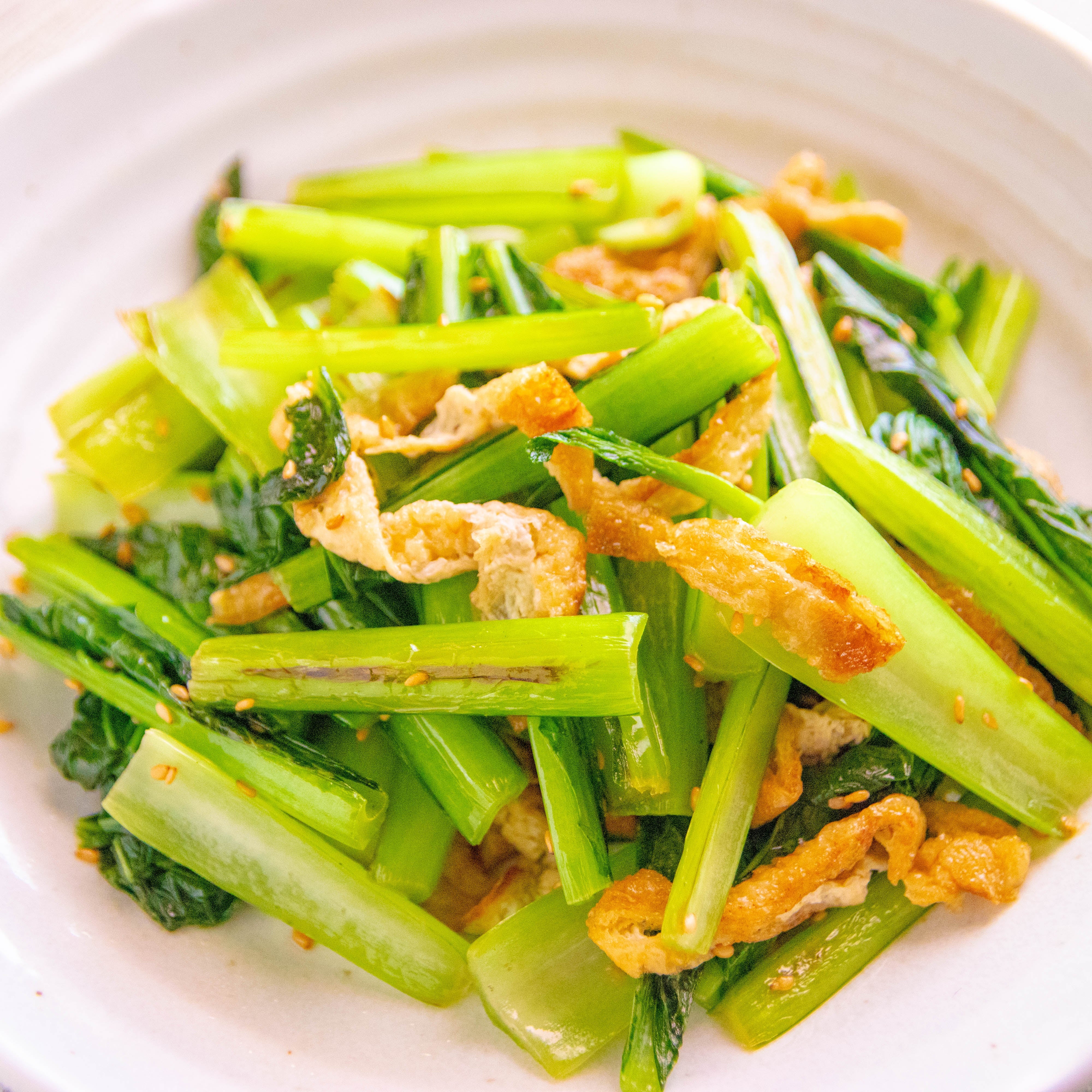 白い皿に盛り付けられた、ツヤのある小松菜とこんがり焼けた油揚げの炒め物。