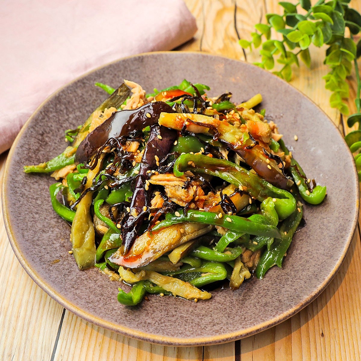 お皿に盛られた野菜炒め。ナスやピーマンが見える。背景に植物の装飾。