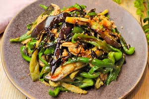 お皿に盛られた野菜炒め。ナスやピーマンが見える。背景に植物の装飾。