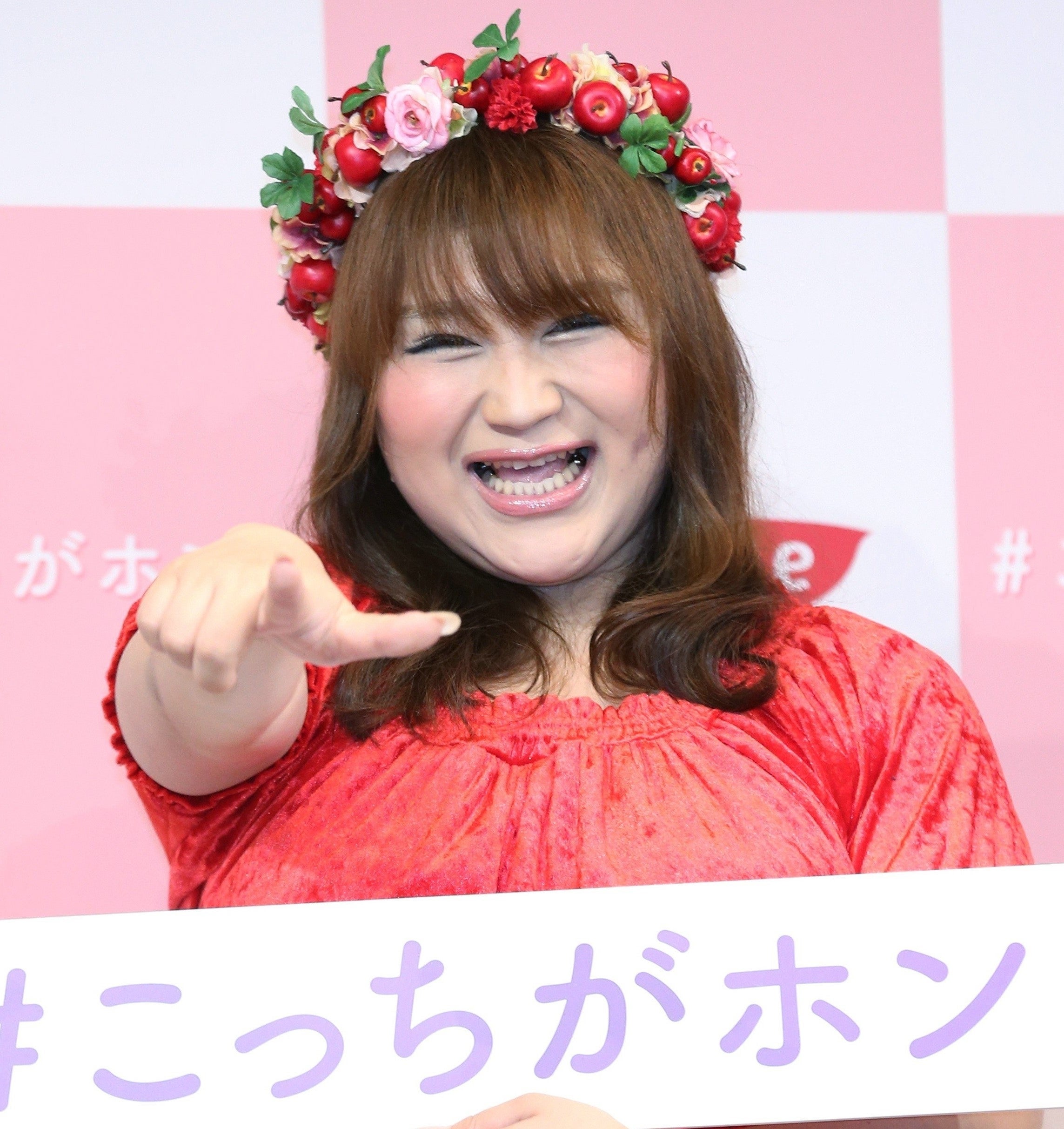 女性が赤い花飾りをつけ、笑顔で指を指している姿。