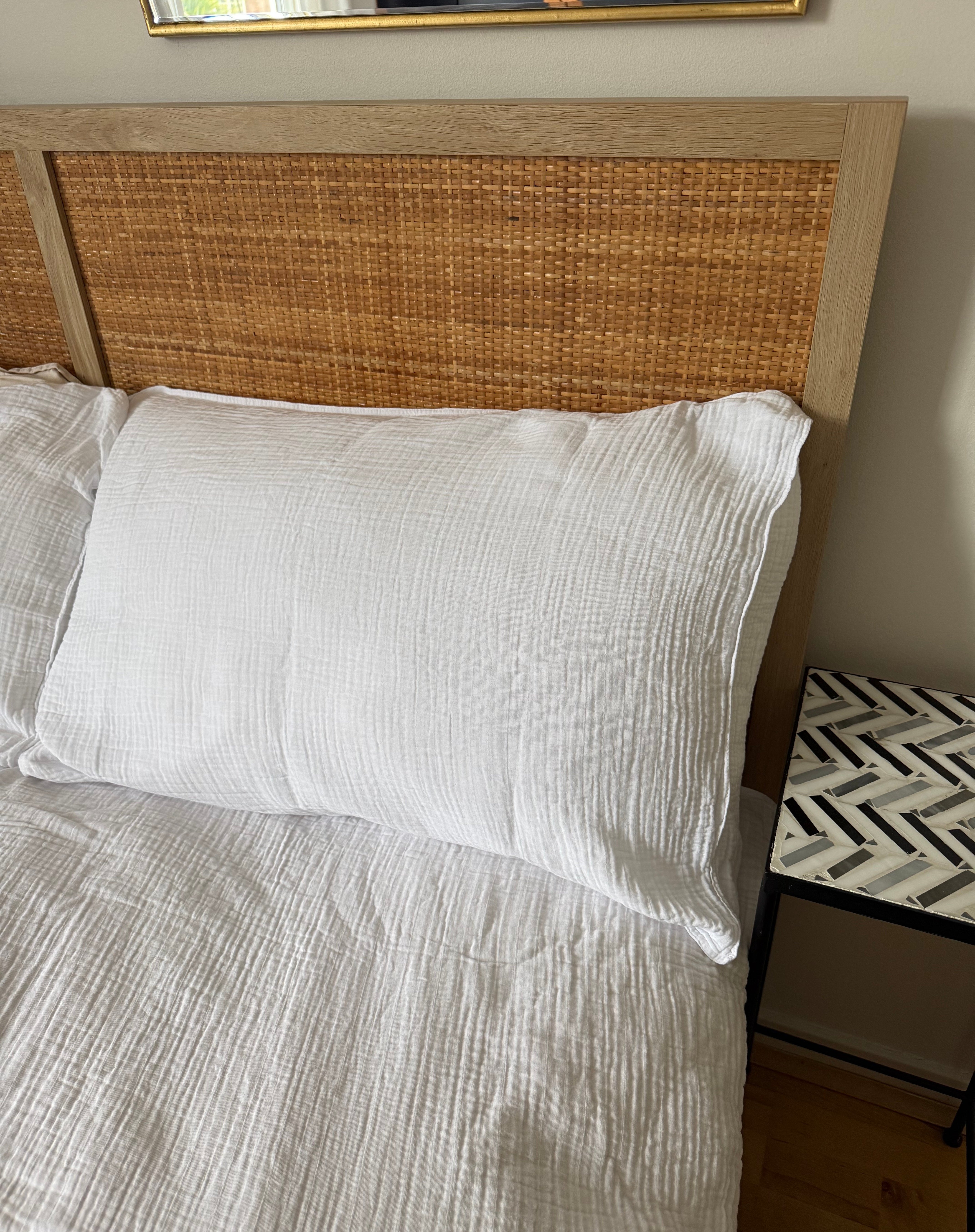 Headboard anyaman dan sarung bantal bertekstur putih di atas tempat tidur yang tertata rapi