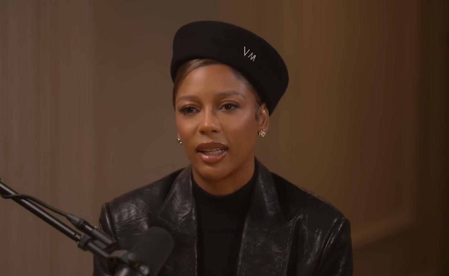 Person successful  a achromatic  leather overgarment   and beret speaks into a microphone during an interview