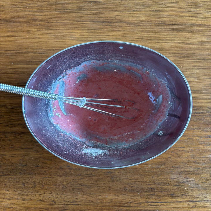 A whisk in a bowl of partially mixed pink batter on a wooden surface