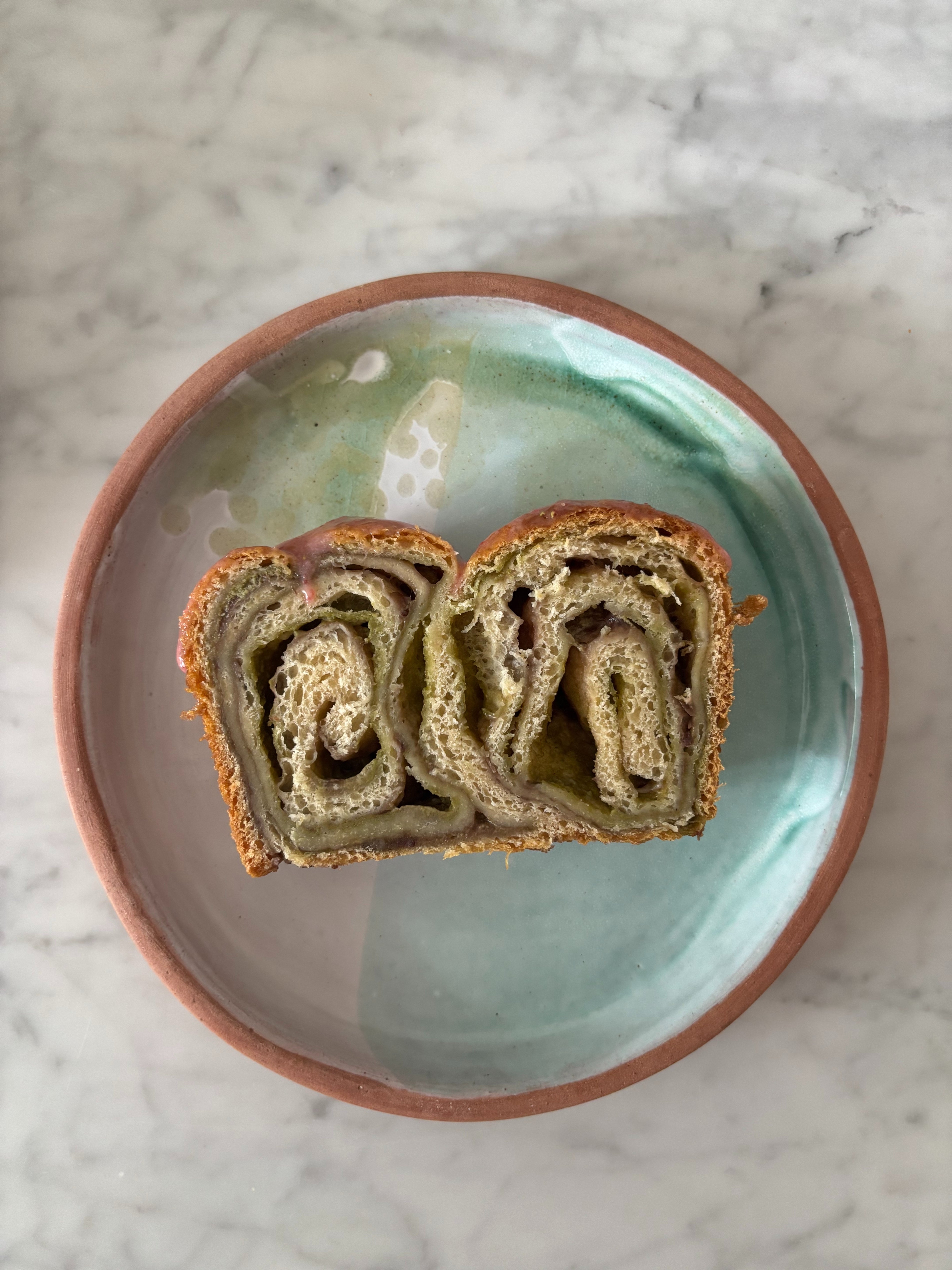 A slice of swirled bread on a round, glazed ceramic plate with a marble background