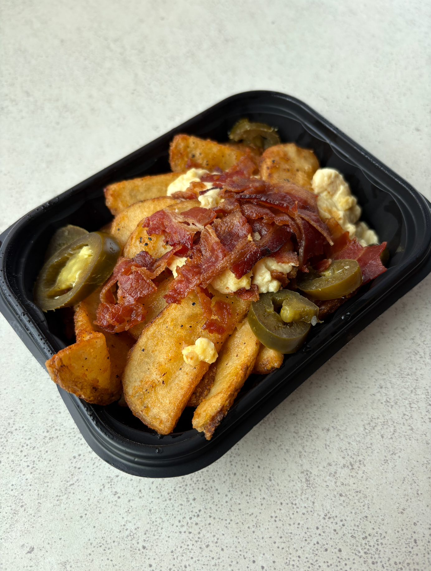 Wendy's jalapeño breakfast potatoes with bacon, cheese sauce, and jalapeños in a black tray on a flat surface