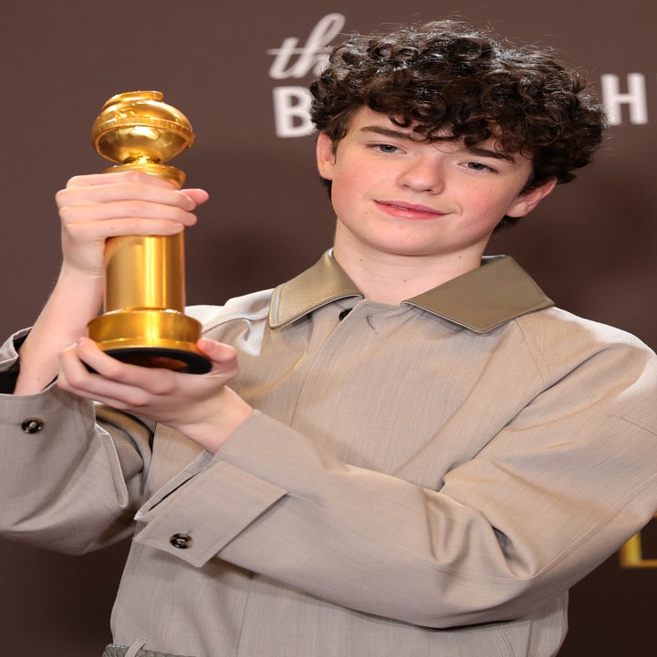 Pessoa segurando um Globo de Ouro, vestindo uma camisa de manga comprida, posando para fotos em um evento de premiação