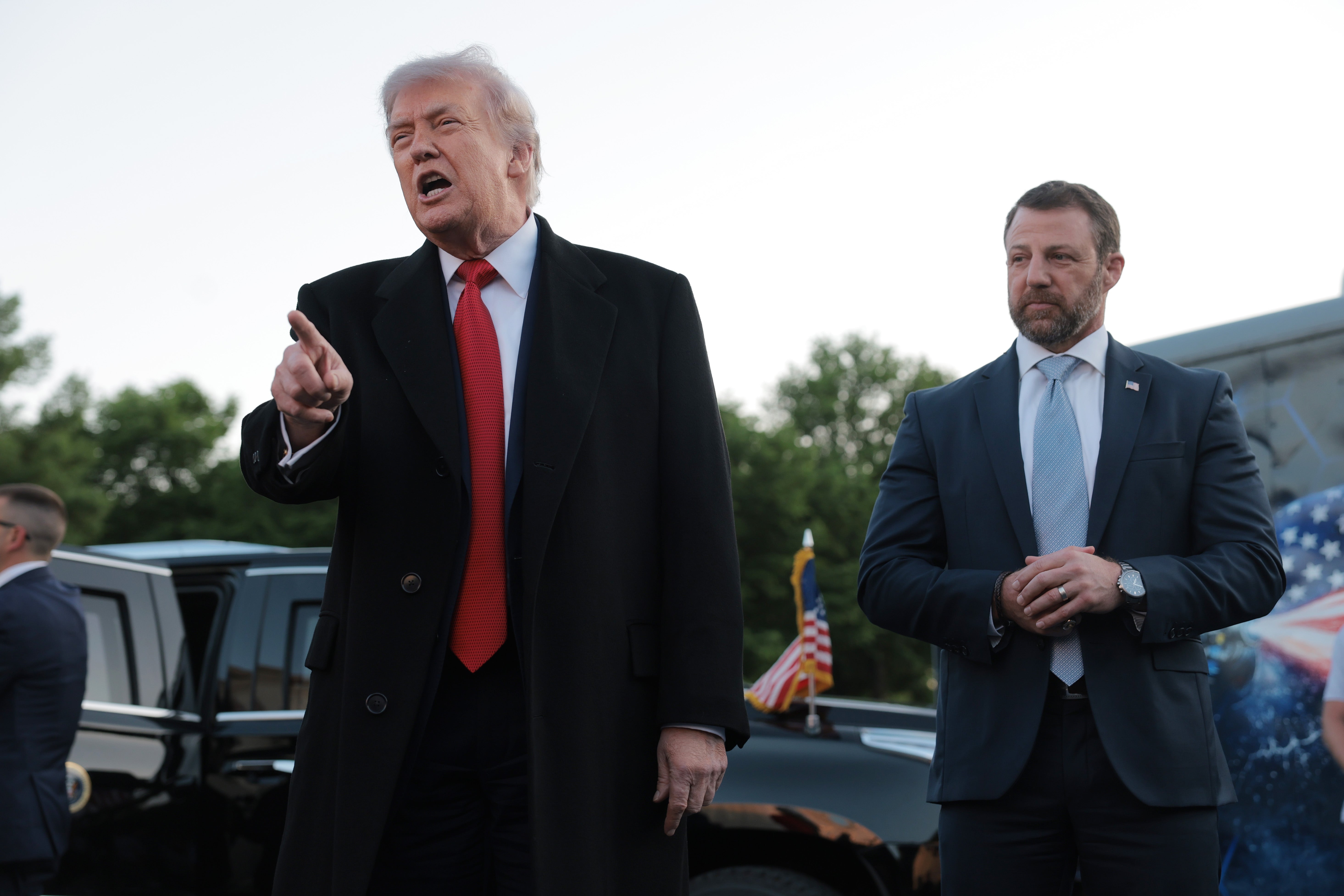 Two men basal outdoors. The antheral connected the near gestures portion wearing a suit with a coat. The antheral connected the close wears a suit, lasting adjacent a vehicle