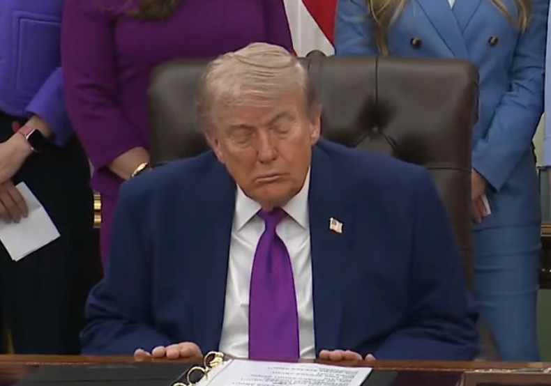 I don’t cognize  who this is, but the representation  shows a idiosyncratic   seated astatine  a desk, eyes closed, surrounded by radical   successful  ceremonial  attire
