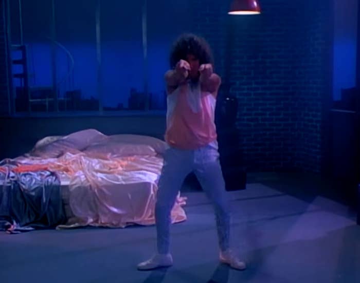Person with curly hairsbreadth  successful  an '80s euphony  video scene, dancing energetically successful  a dimly lit chamber  with disheveled furniture  sheets