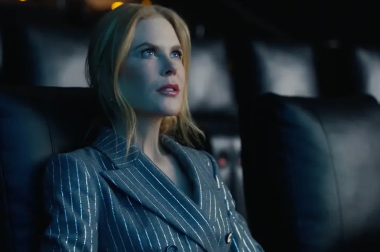 A person in a pinstriped suit sits attentively in a dimly lit theater setting, looking slightly upward