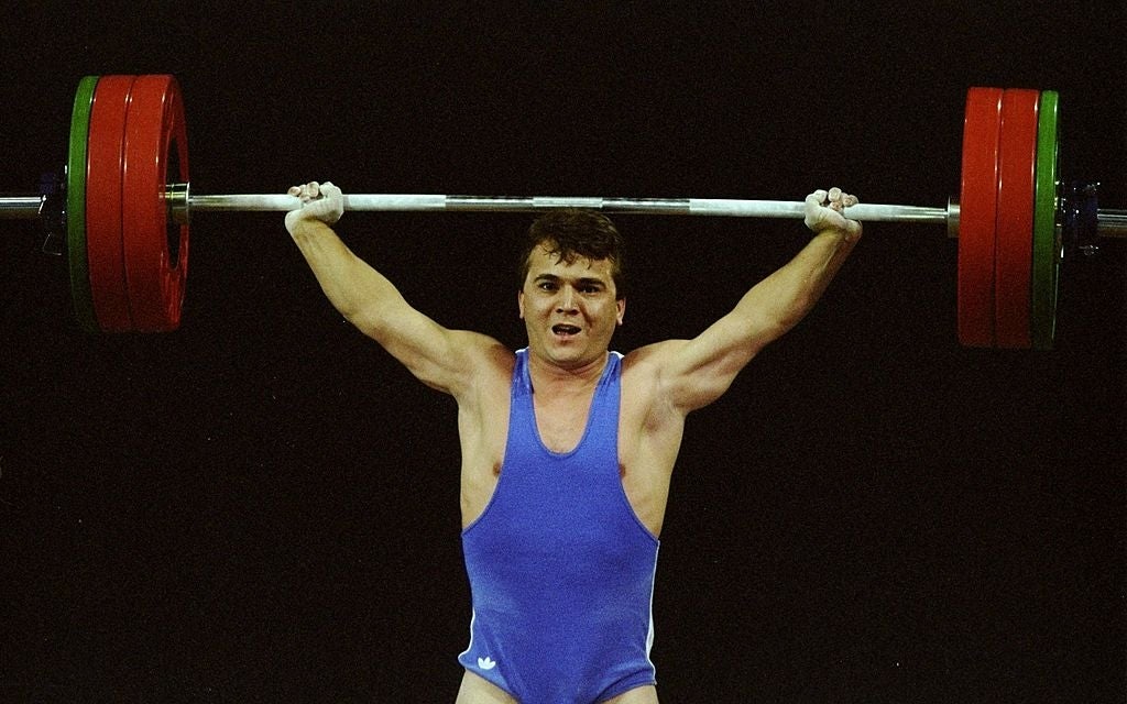 Person lifting a dense  barbell overhead during a weightlifting competition, wearing a bluish  singlet, showcasing spot    and focus