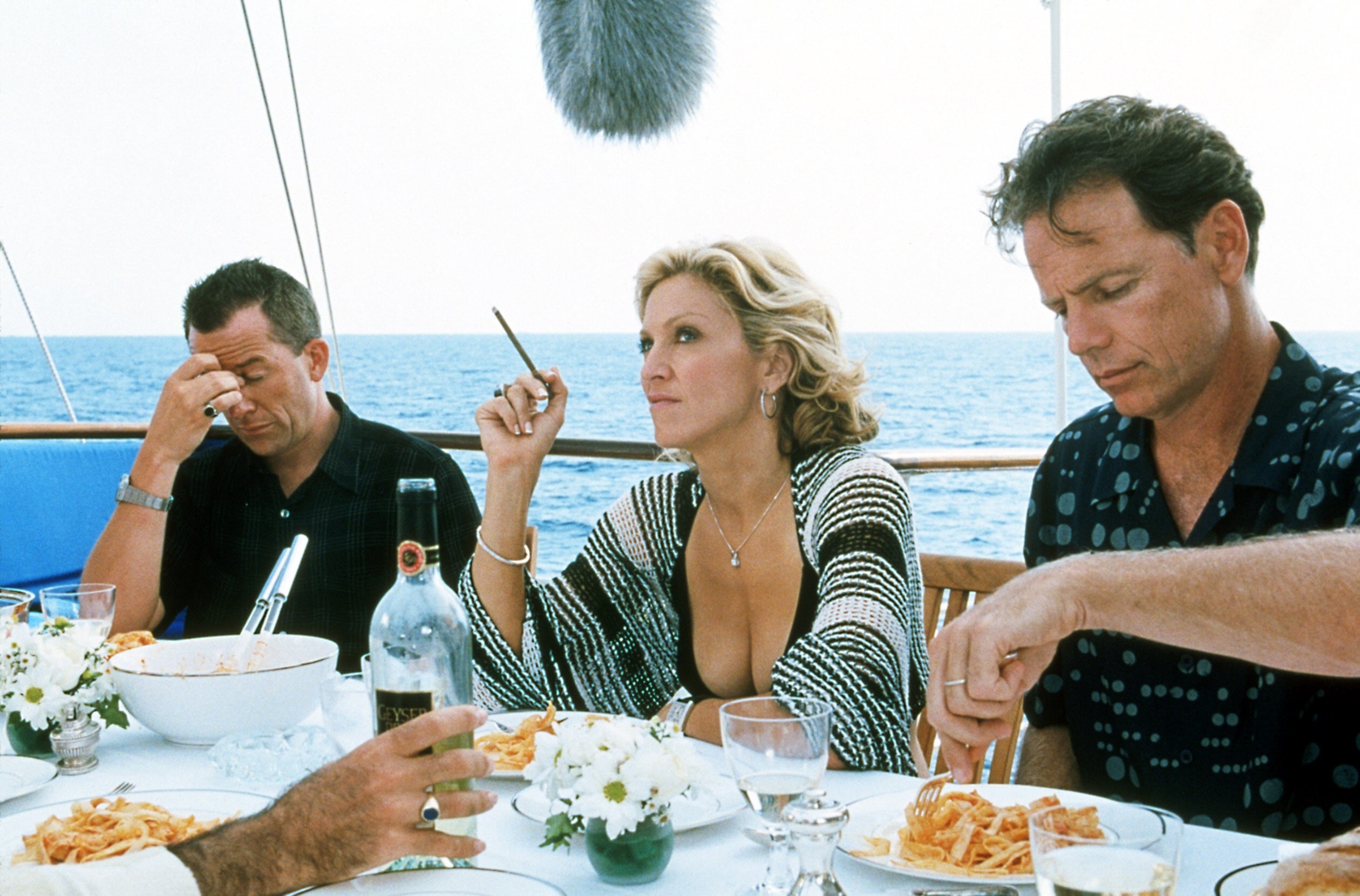 People eating connected a yacht, 1 idiosyncratic holds a cigaret contemplatively, with plates of pasta and vino connected the table