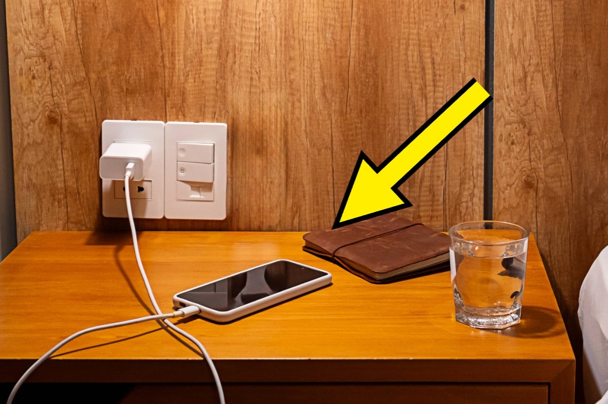 Smartphone charging on nightstand next to a leather wallet and a glass of water