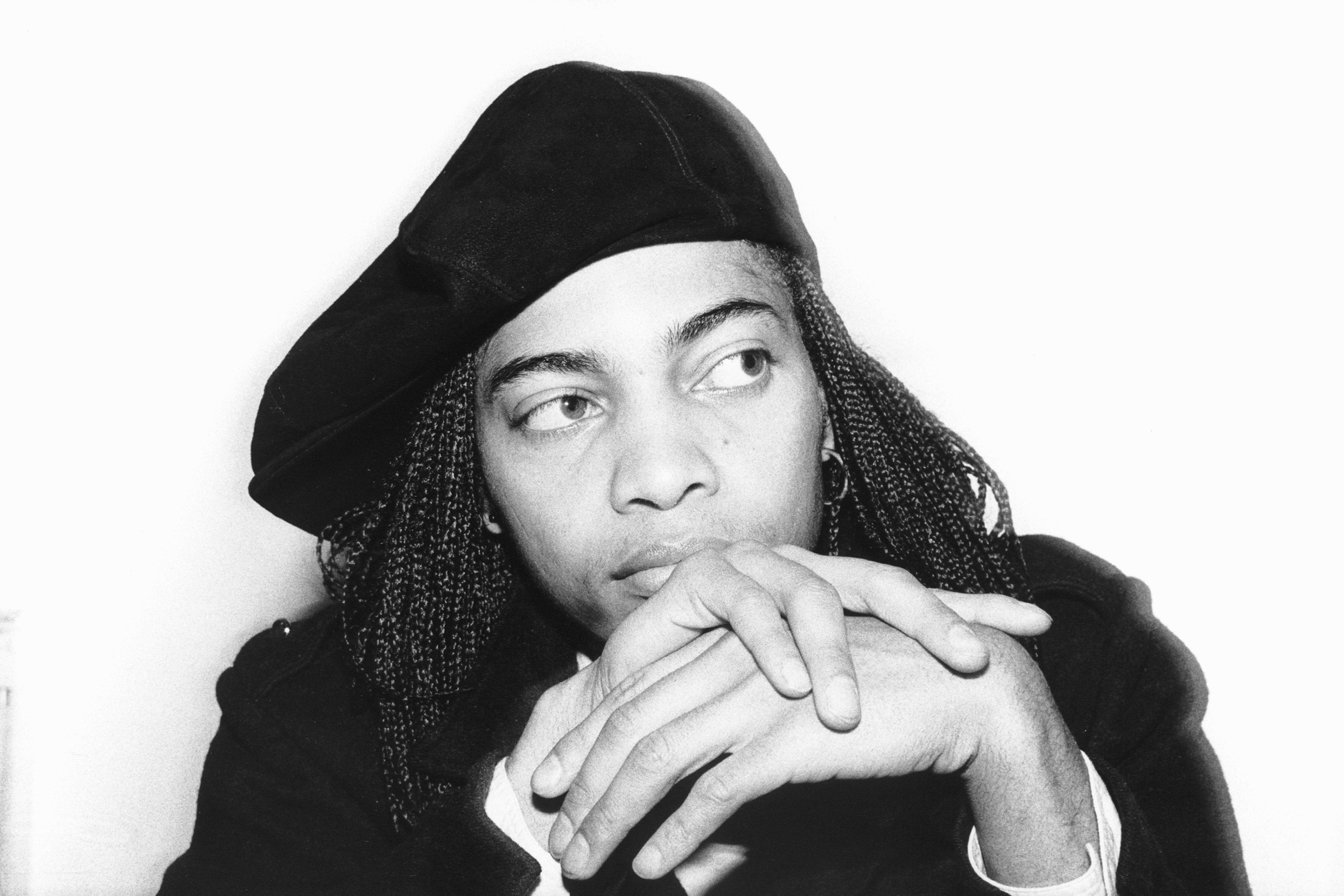 Person wearing a beret and braided hairstyle, looking thoughtful with hands clasped adjacent face