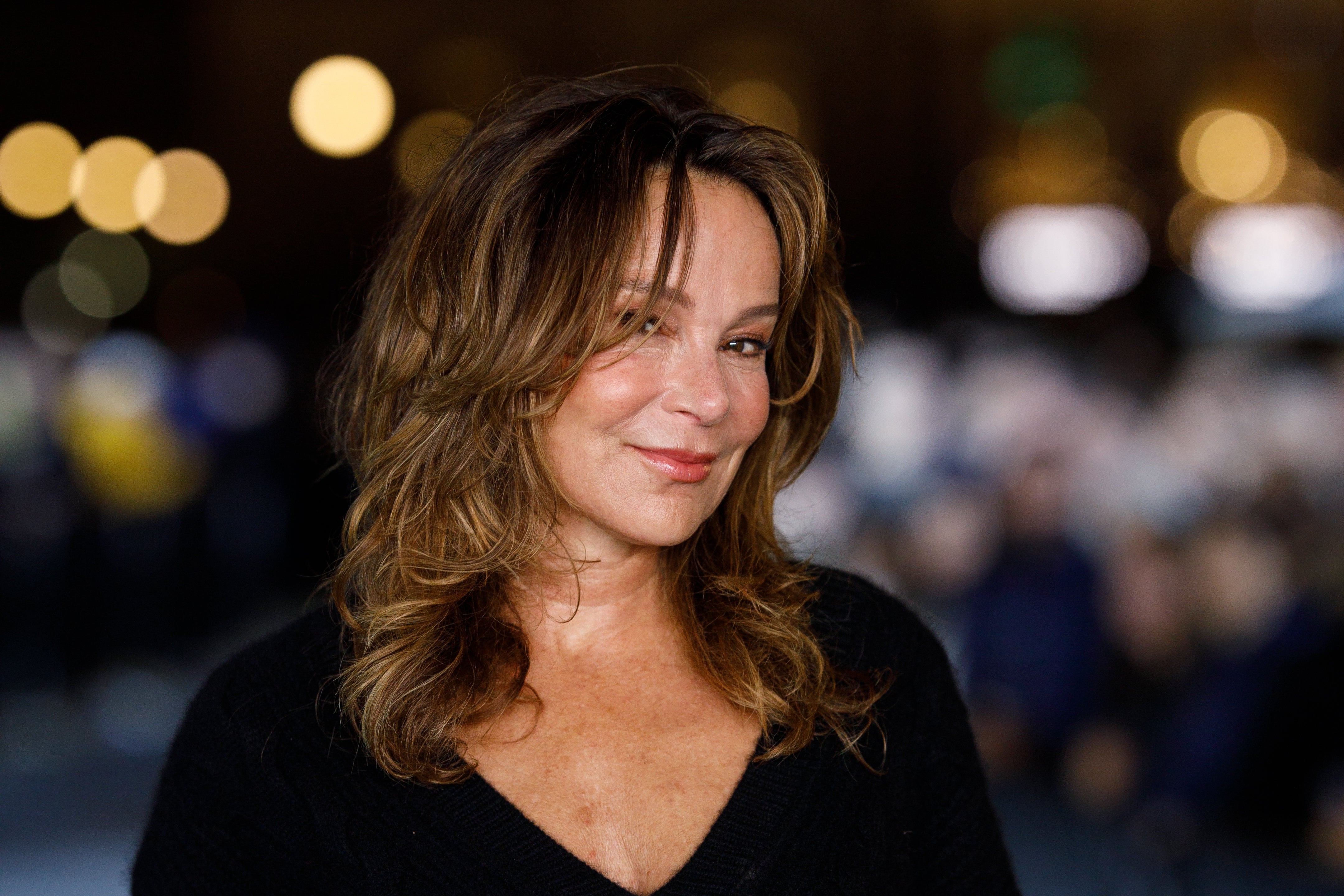 Person posing connected reddish carpet successful elegant achromatic outfit, with agelong wavy hair, smiling subtly astatine the camera