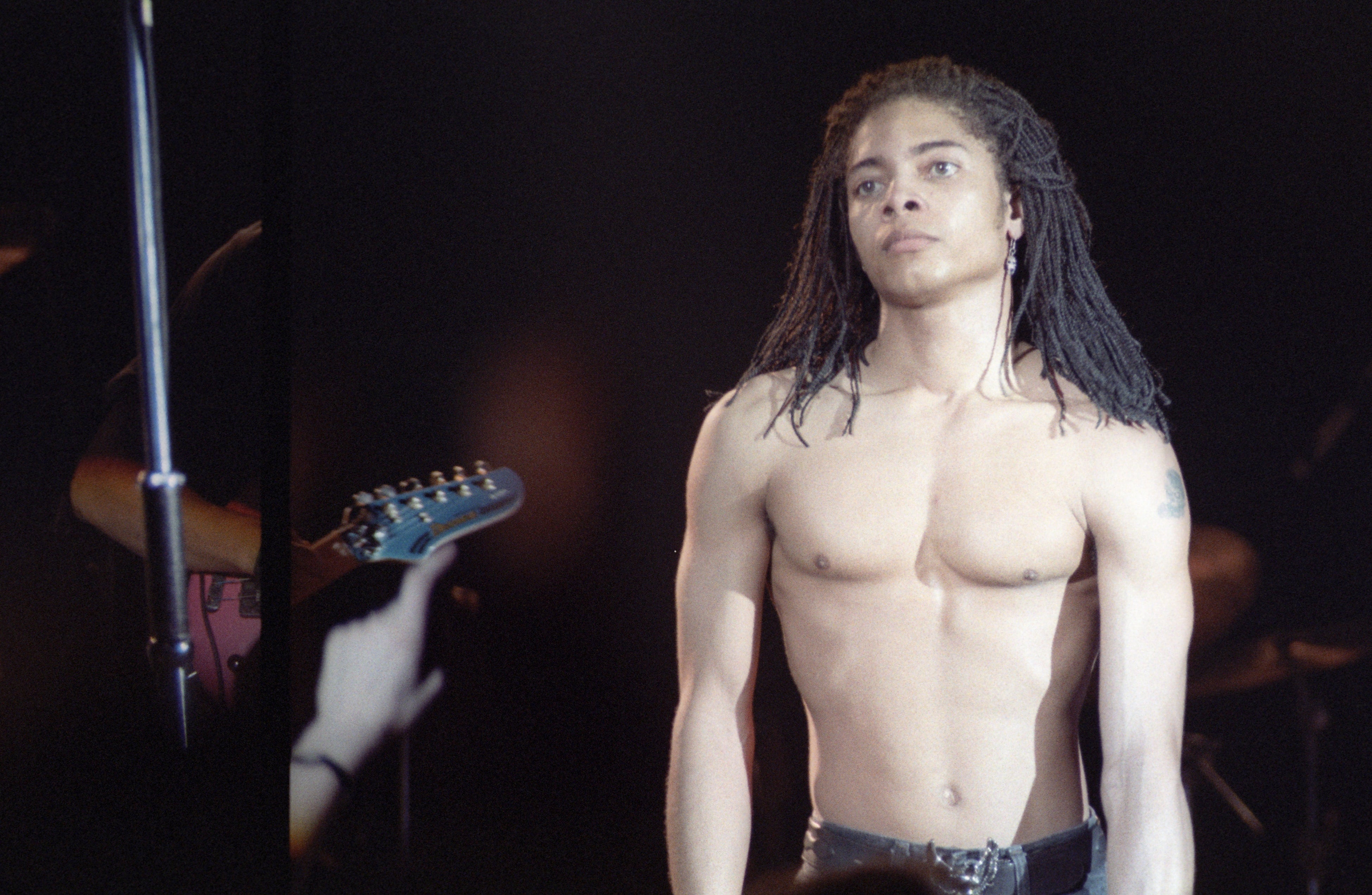 Musician with agelong braids stands shirtless connected signifier during a performance