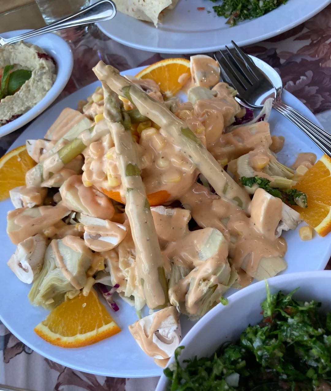 Plate of salad with asparagus, artichokes, orange slices, and dressing. Accompanied by hummus and tabbouleh in small bowls