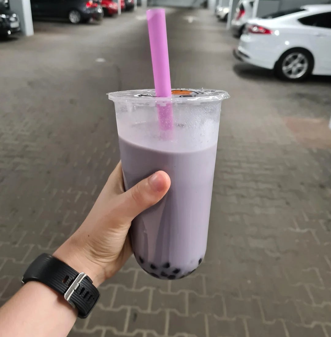Hand holding a cup of bubble tea with a straw, in a parking garage setting