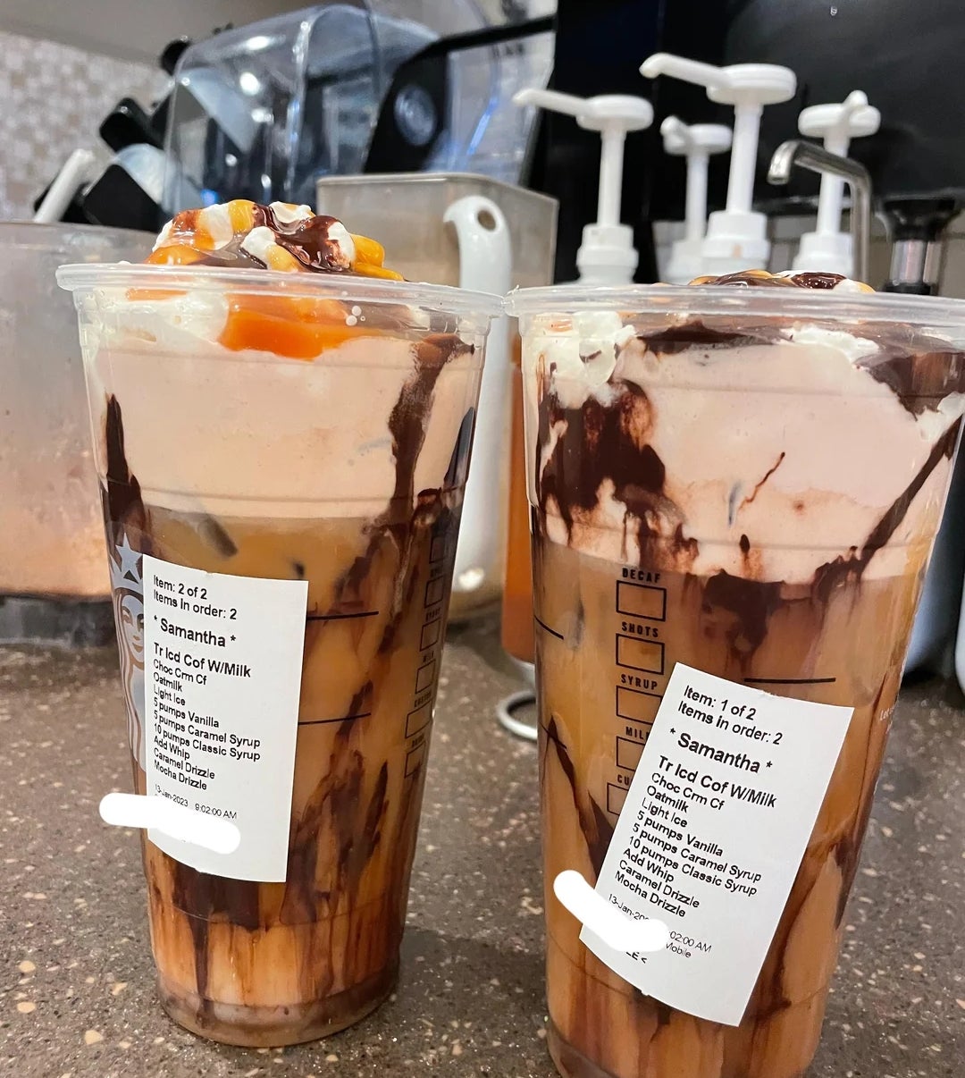 Two iced coffee drinks topped with whipped cream, caramel drizzle, and chocolate syrup, labeled with customization details on the cups