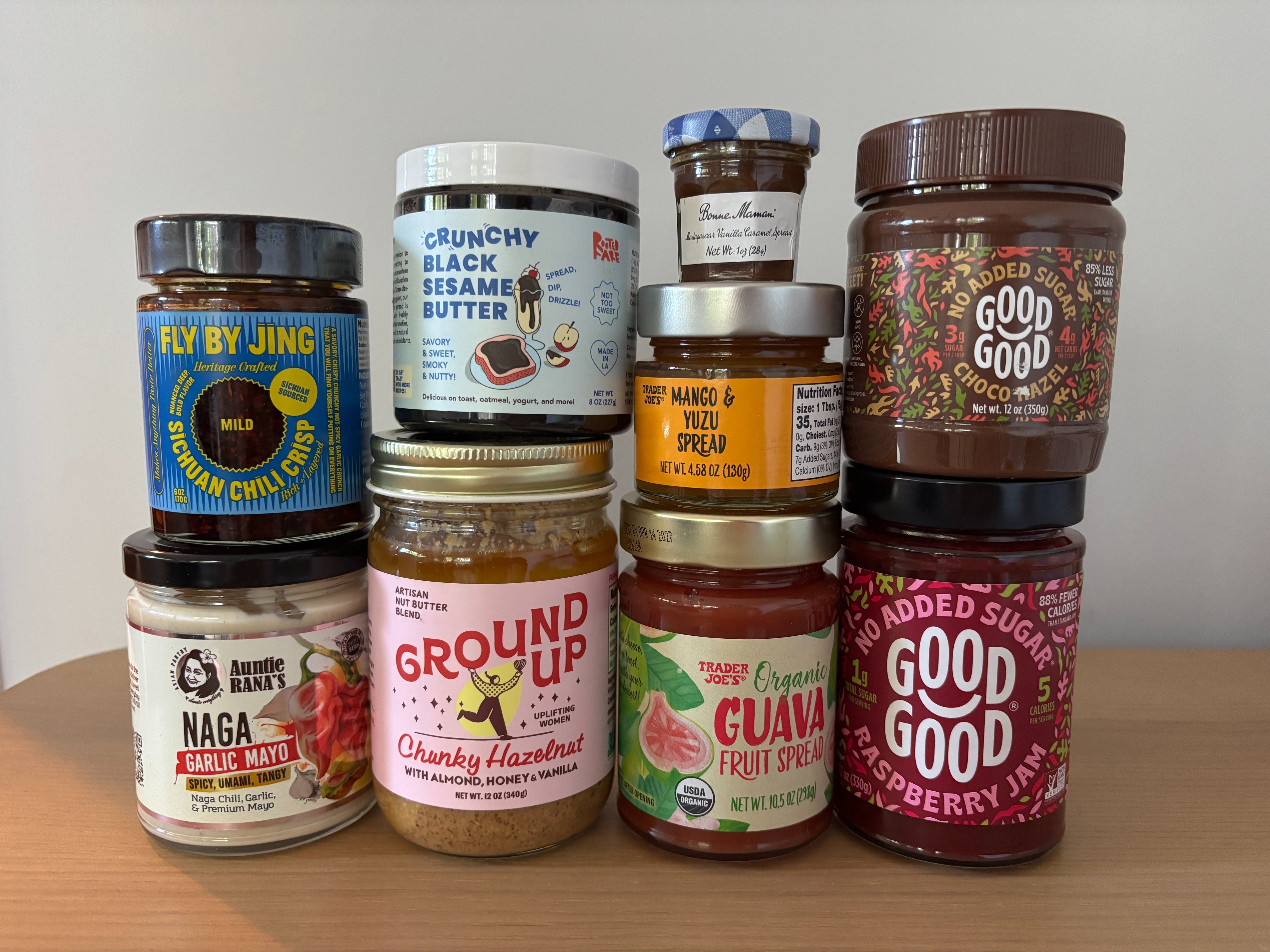 A variety of jars containing different spreads and butters are stacked on a wooden surface