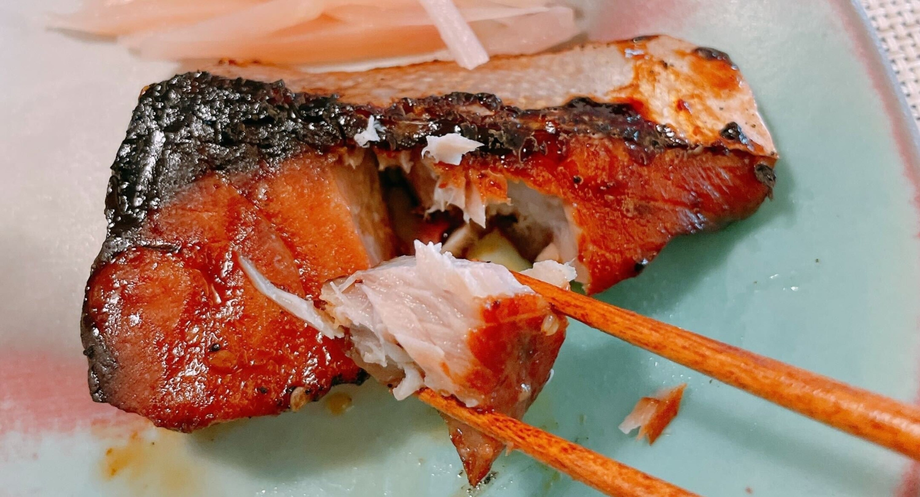 焼き魚が箸でほぐされた状態で皿に盛られ、大根のつまが添えられているシーン。