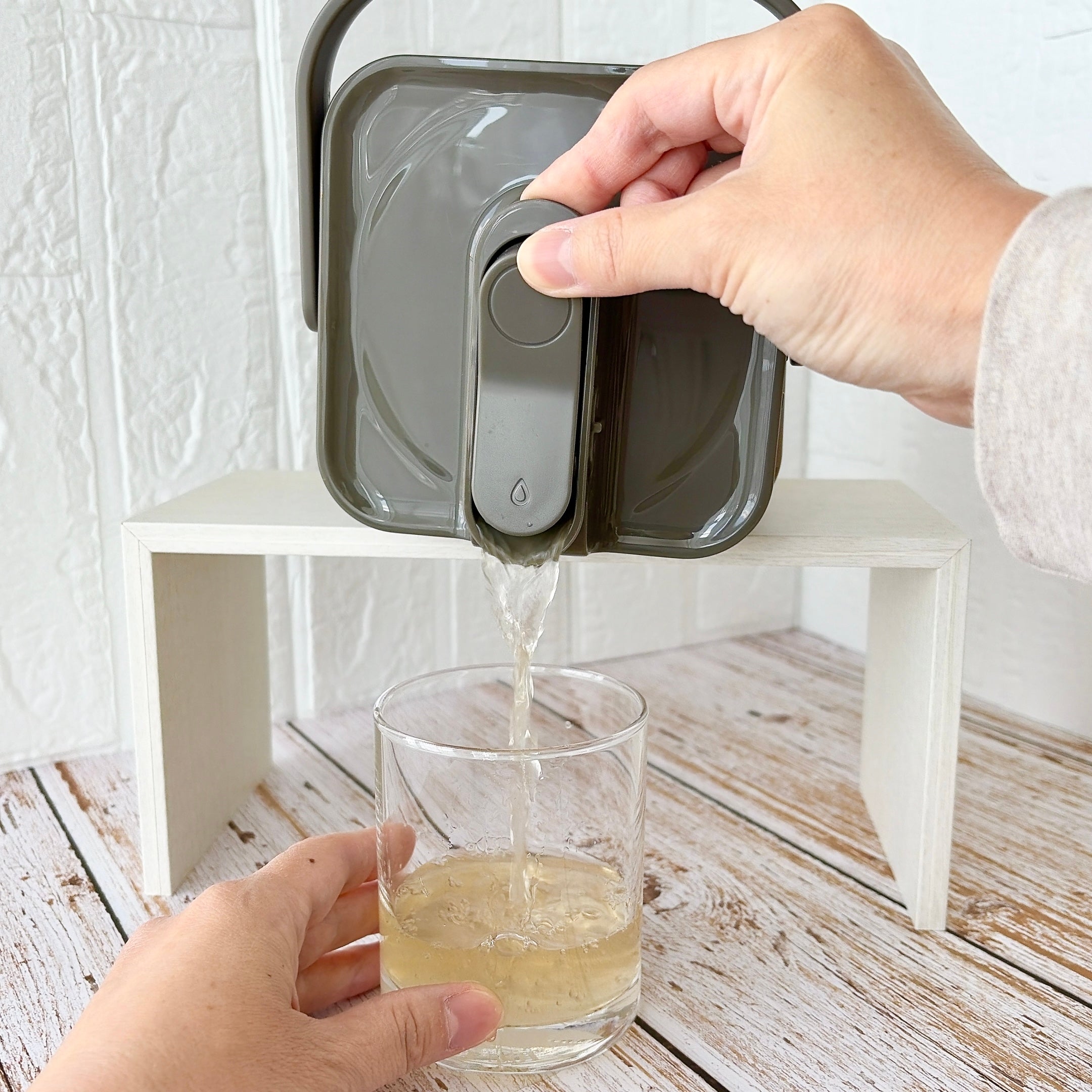3COINS（スリーコインズ）「ドリンクサーバー：2.3L／KITINTO」手を使ってディスペンサーからグラスに飲み物を注いでいる様子。