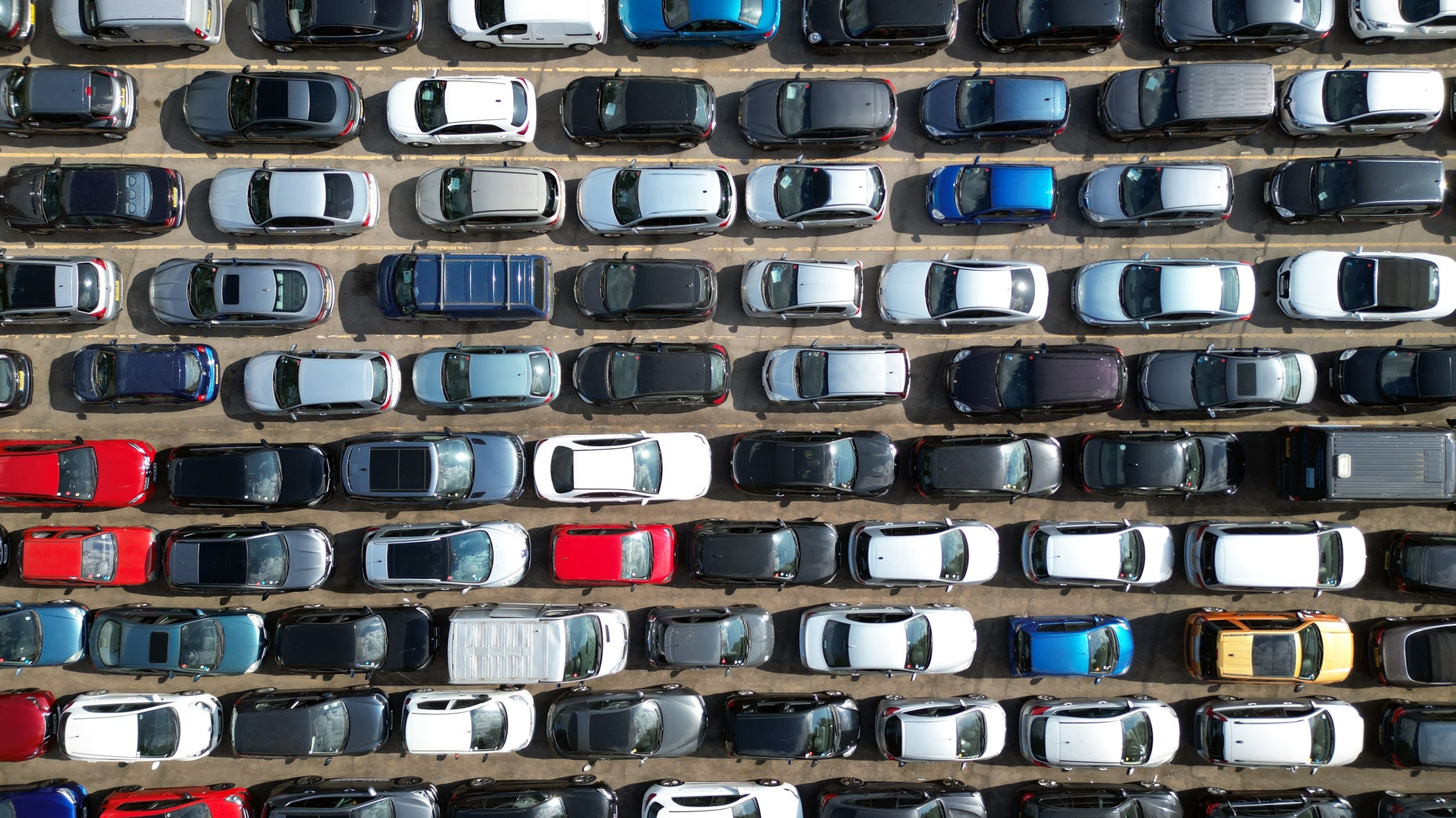 Luftfoto av en tettpakket parkeringsplass fylt med forskjellige parkerte biler, som illustrerer urban overbelastning og etterspørsel etter bilplasser
