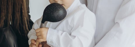 大人のサポートを受けながら、木製のボウルにおたまを使っている子ども。