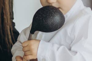 大人のサポートを受けながら、木製のボウルにおたまを使っている子ども。