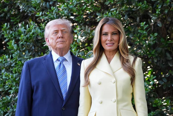 Two radical   basal   outdoors; 1  successful  a suit   and tie, the different   successful  a light-colored, double-breasted coat, some  looking astatine  the camera