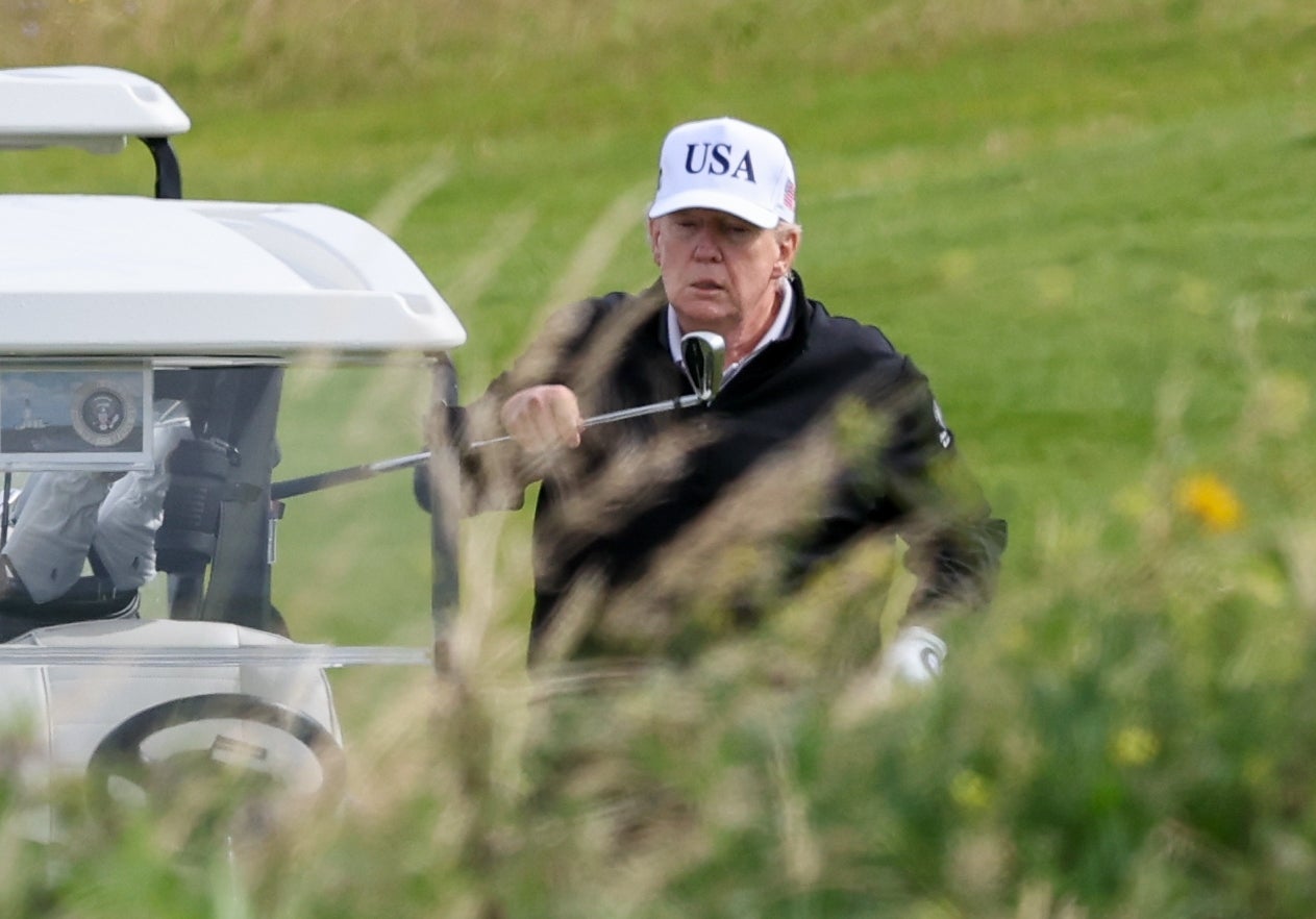 Person i en golfbil som holder en kølle, iført USA-hette. Gress i forgrunnen