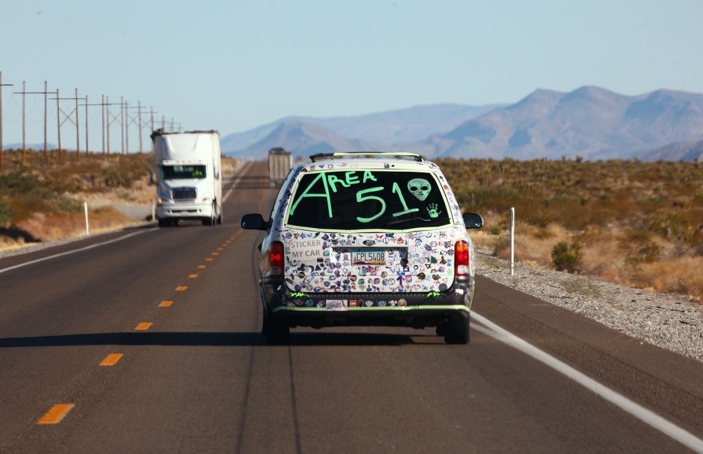 Minivan på ørkenmotorveien med "Area 51" og fremmed ansikt malt på bakruten, klistremerker som dekker kjøretøyet