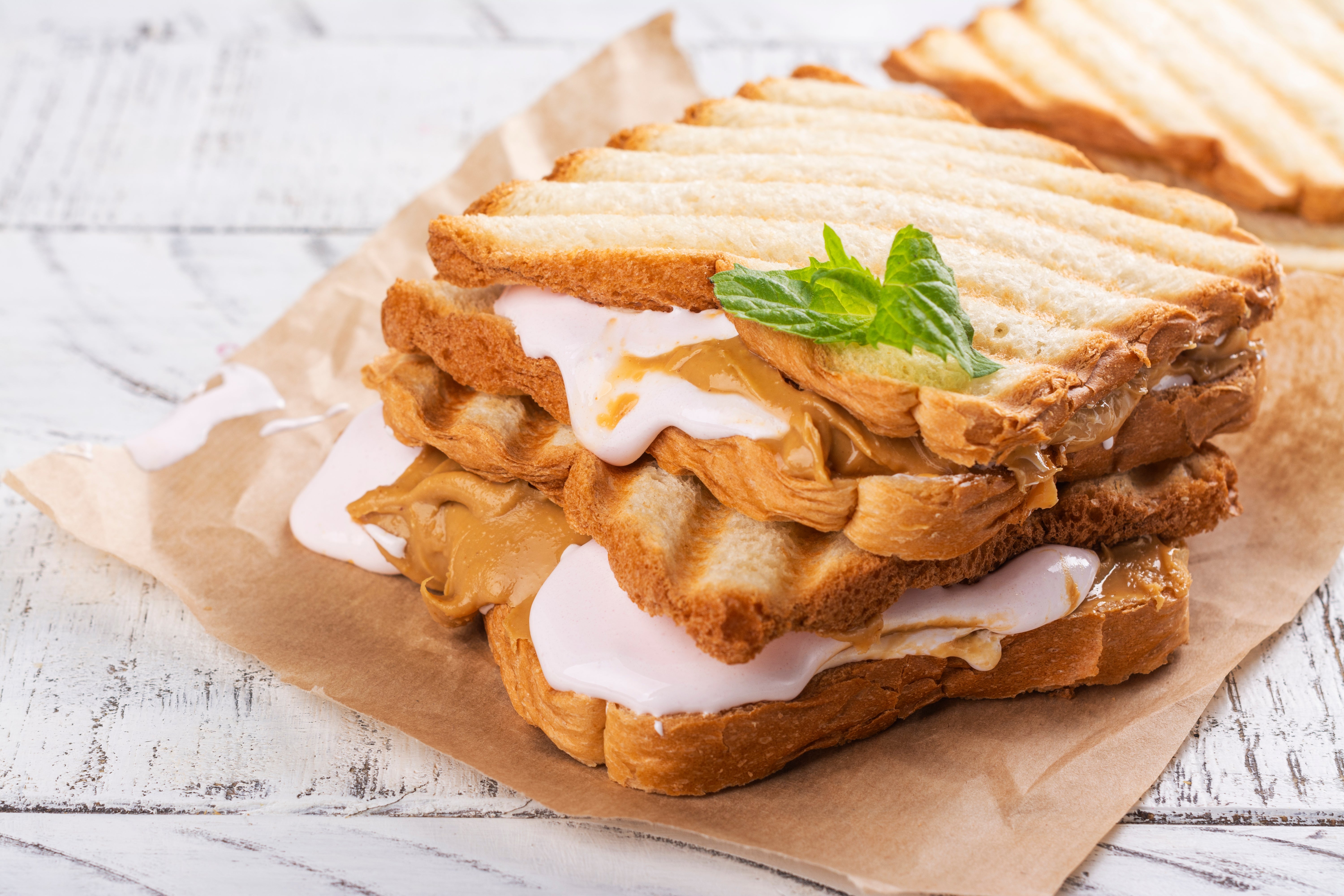Grilled sandwich with peanut butter and melting marshmallow cream, garnished with a mint leaf, on brown paper
